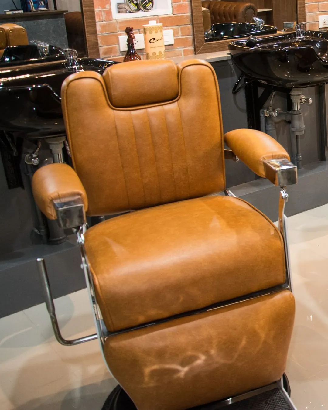Fauteuils de barbier en cuir camel alignés devant les miroirs